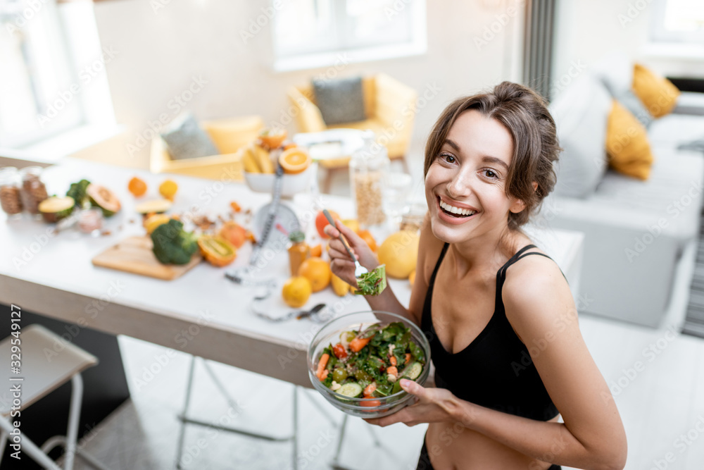 Portrait of a cheerful athletic woman eating healthy salad during a break at home. Concept of losing