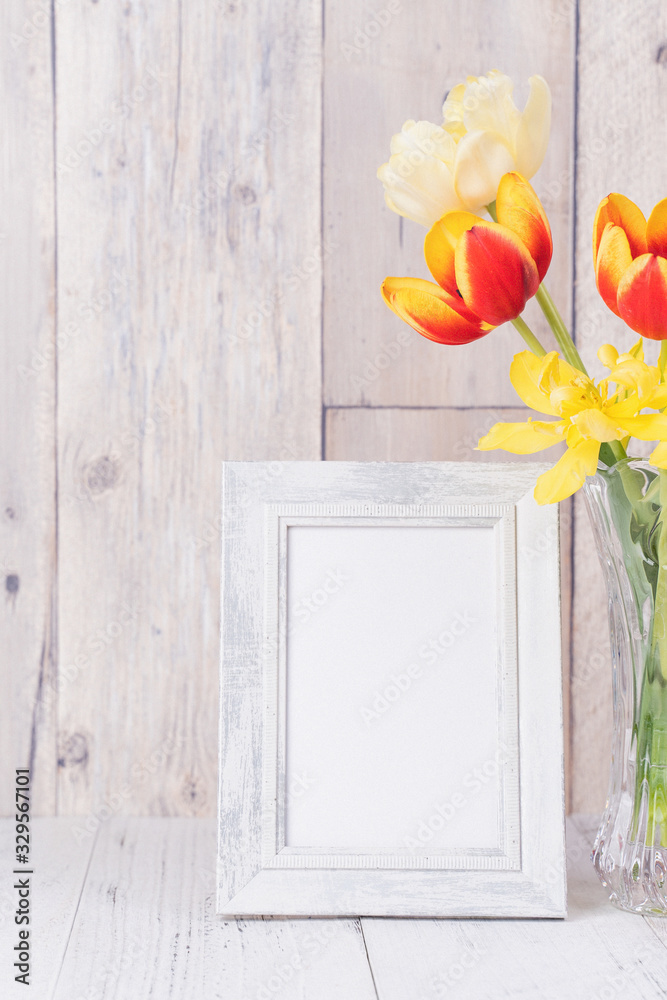 家里木桌背景墙上有相框装饰的玻璃花瓶里的郁金香花，关闭u