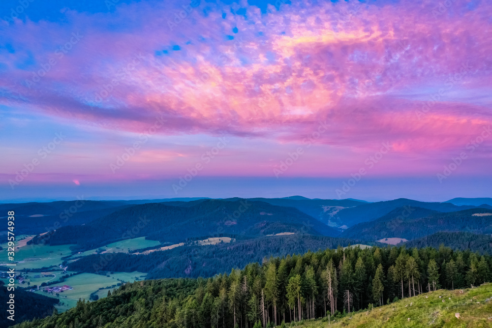 Colorful sunset, green mountains and grass, and sky with clouds above the forest