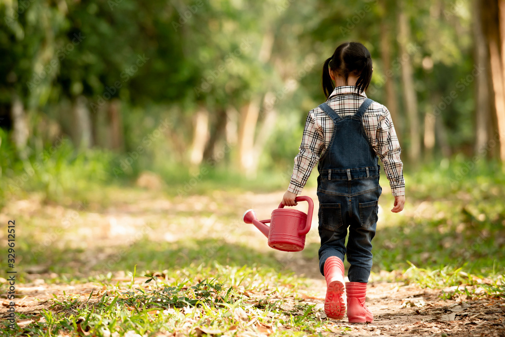亚洲小女孩拿着水罐走进公园的背面