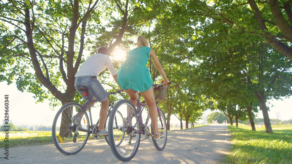 LOW ANGLE: Couple enjoys an active date by riding bikes down a sunlit avenue