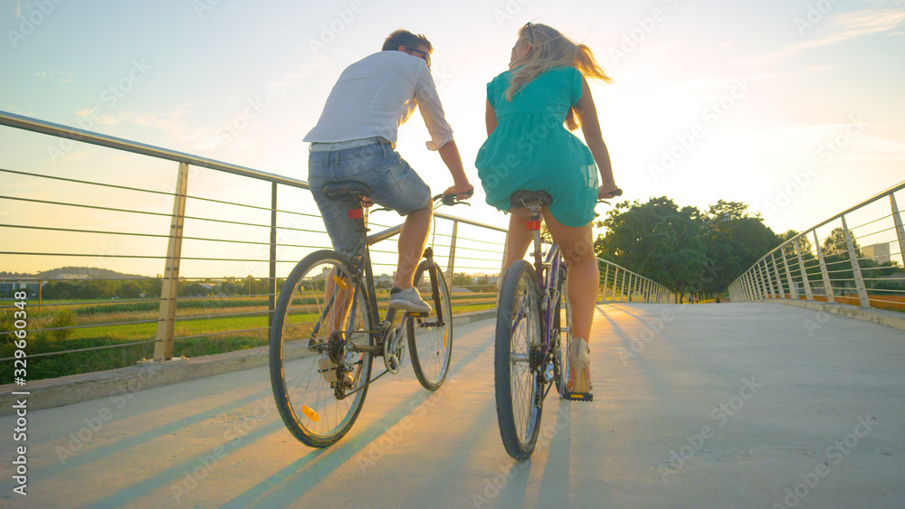 LOW ANGLE: Unrecognizable couple riding their bikes across an overpass at sunset
