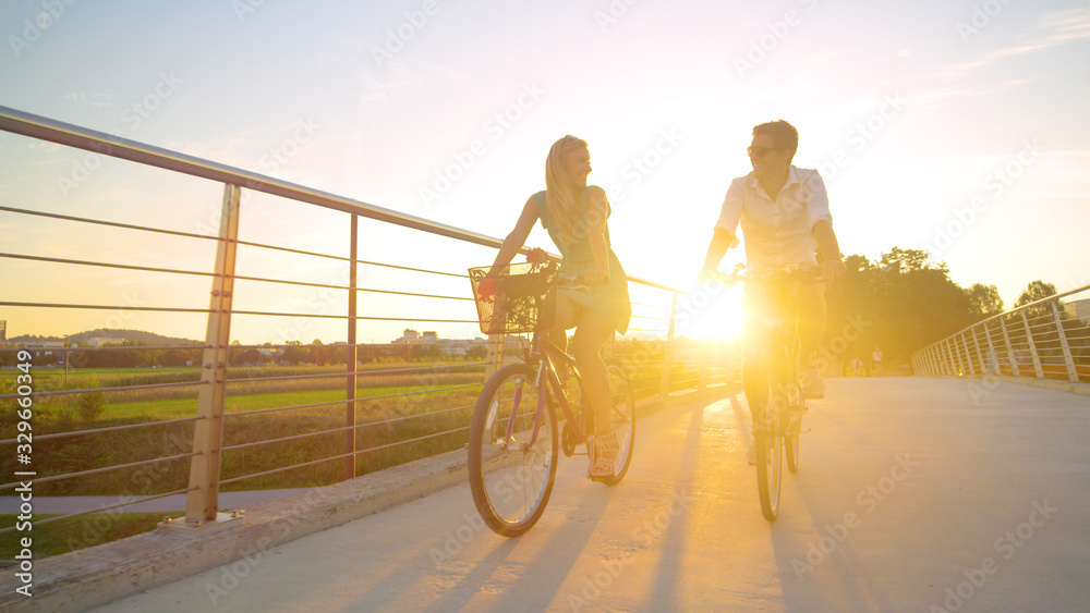 LOW ANGLE: Young woman smiles while riding her bike with her boyfriend at sunset