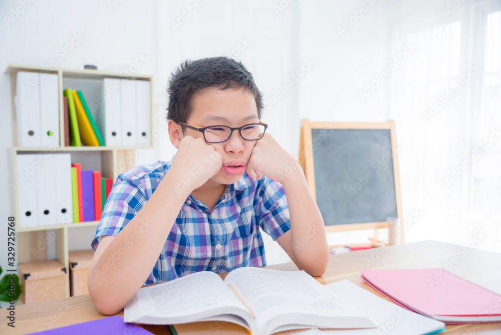 年轻的亚洲男孩因为看书或做作业而感到疲惫和困倦。