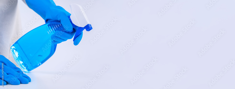 年轻的女管家正在用蓝色手套、喷雾清洁剂、湿的围裙清洁白色桌子
