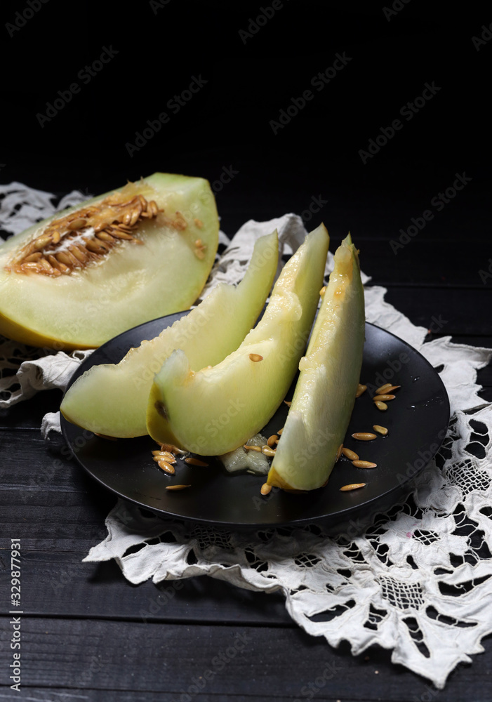 Ripe melon slices in black plate and half of melon aside on white handymade napkin lying at wooden t
