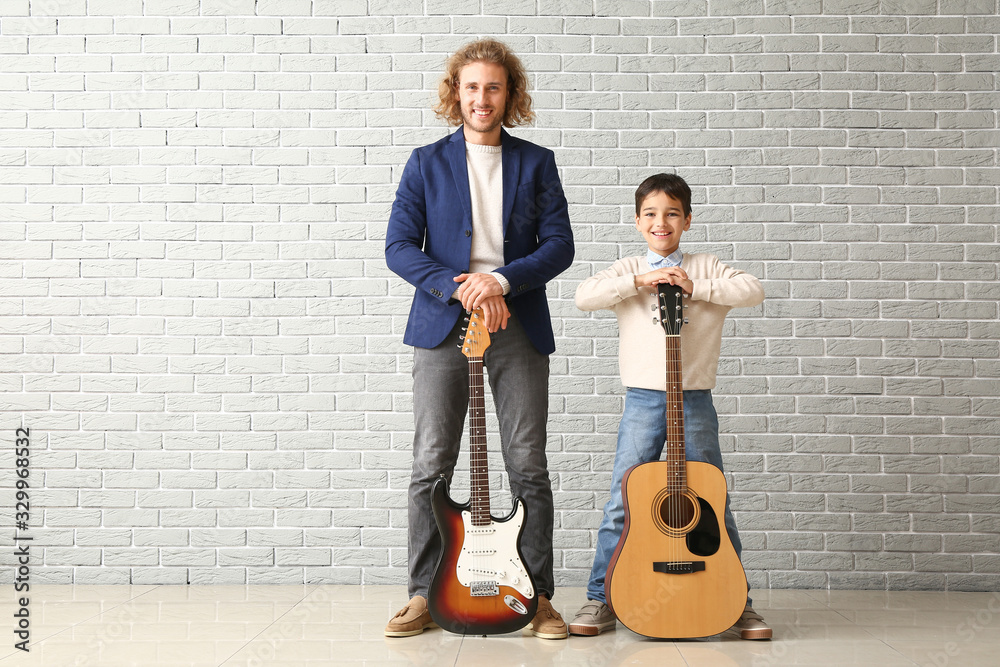 一个男人和他的小儿子靠着砖墙拿着吉他