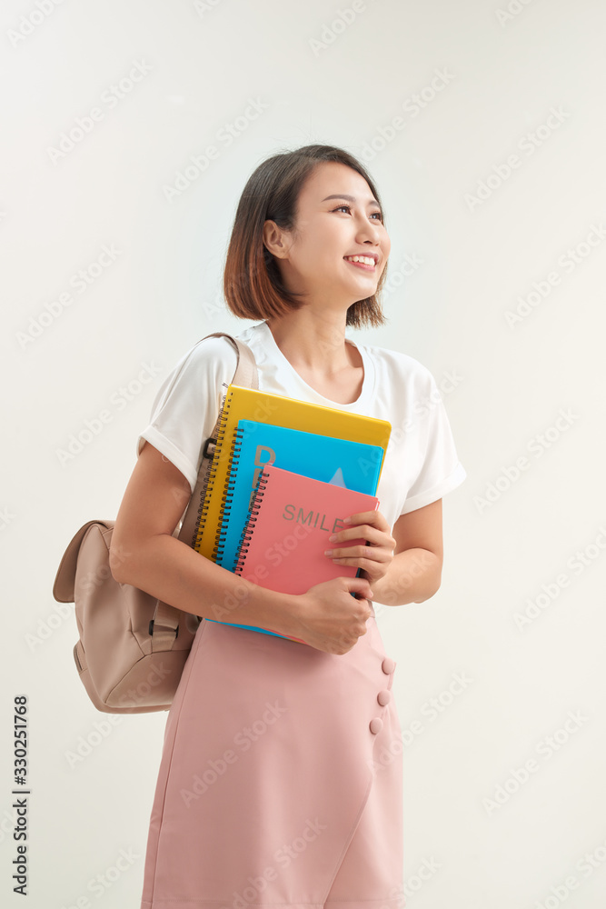 背着背包的年轻亚洲女学生拿着隔离在白色背景上的书工作室肖像