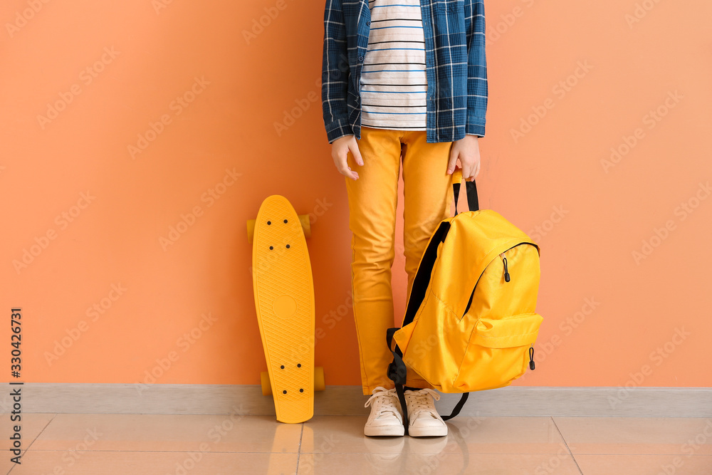 Cute little boy with skate and backpack near color wall