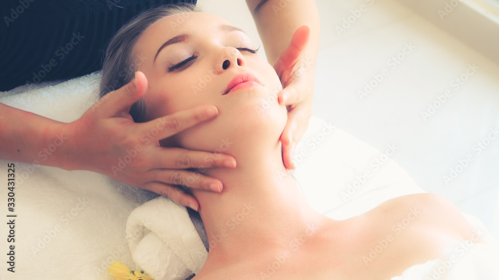 Relaxed woman lying on spa bed for facial and head massage spa treatment by massage therapist in a l