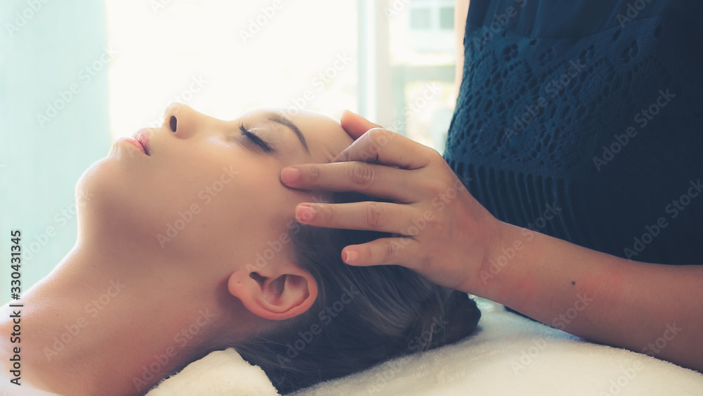 放松的女人躺在水疗床上，接受按摩师的面部和头部按摩水疗