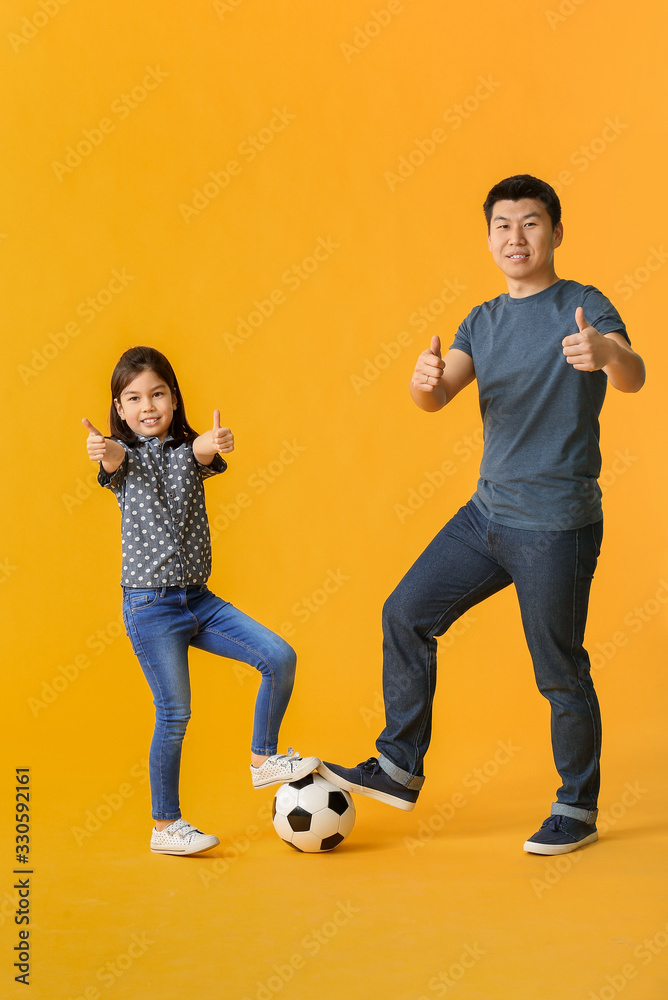 快乐的亚洲男人和他的小女儿，球在彩色背景上竖起大拇指