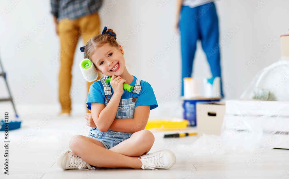 手里拿着油漆滚筒的快乐小女孩和父母一起在公寓里粉刷墙壁