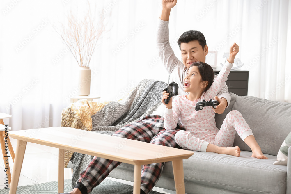 亚洲男子和他的小女儿在家玩电子游戏
