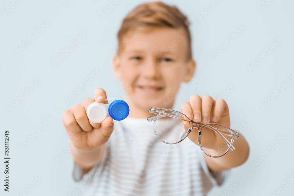 灰色背景下戴着隐形眼镜盒和眼镜的小男孩，特写镜头