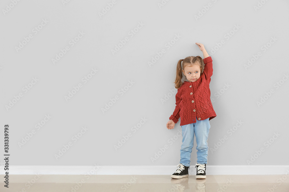 可爱的小女孩在灰色墙壁附近测量身高