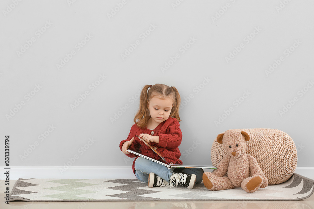 可爱的小女孩在灰色的墙上看书