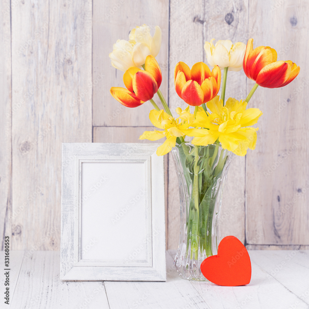 Tulip flower in glass vase with picture frame decor on wooden table background wall at home, close u