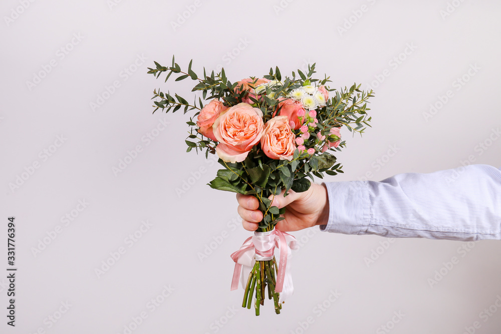 Studio shot of young man wearing cotton shirt, holding beautiful bouquet of pink flowers. Close up, 