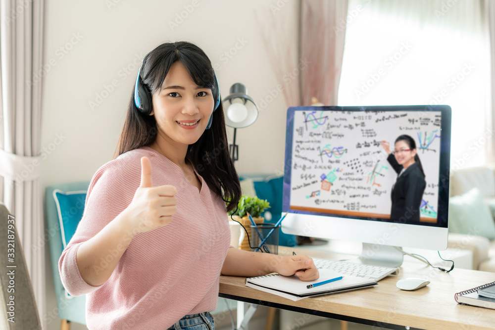 亚洲女学生与老师在电脑上进行视频电子学习，并在家里的客厅竖起大拇指。e