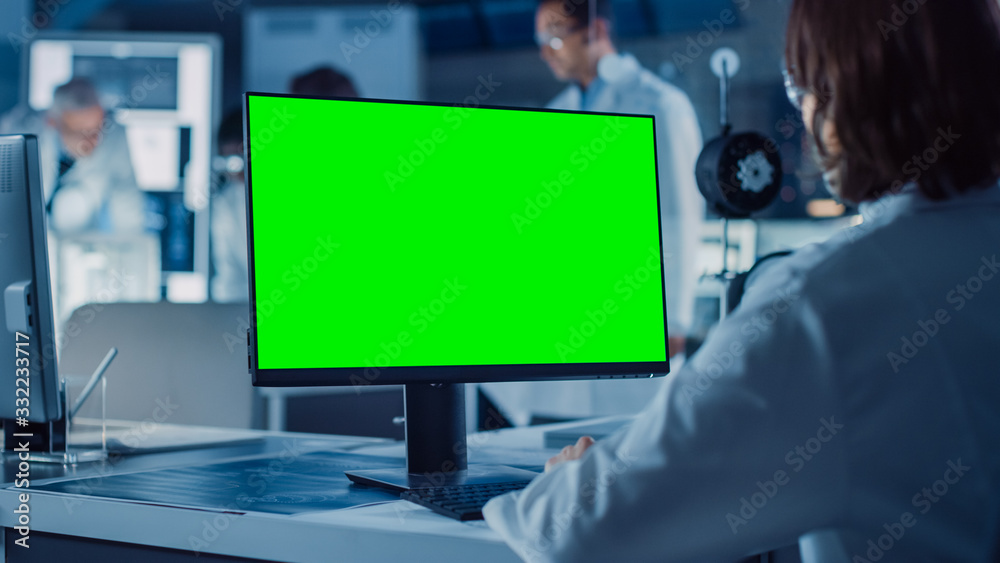 肩上镜头：女IT科学家使用绿色实体屏幕电脑。背景技术
