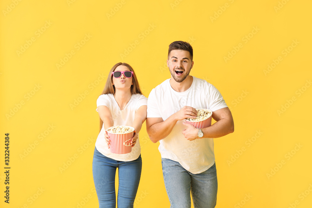 快乐的年轻情侣带着爆米花在彩色背景下看电影
