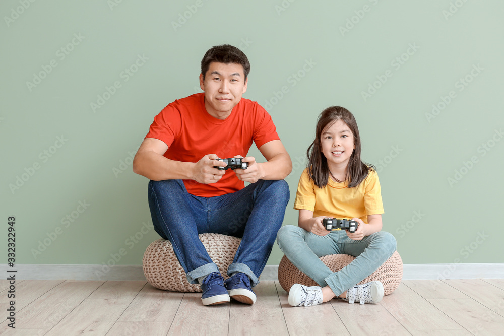Happy Asian man and his little daughter playing video game near color wall