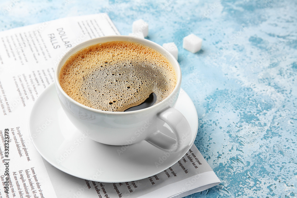 Cup of hot coffee and newspaper on color background