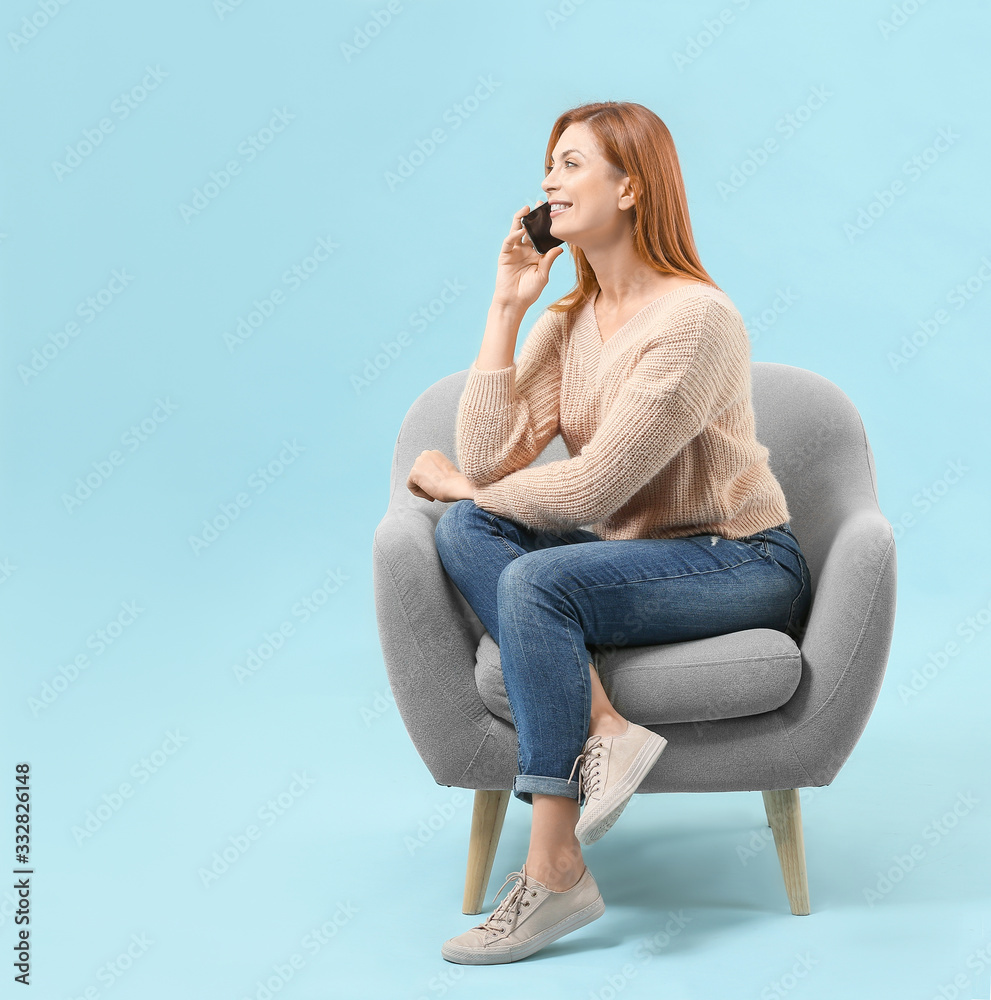 美丽的女人坐在彩色背景的扶手椅上打电话