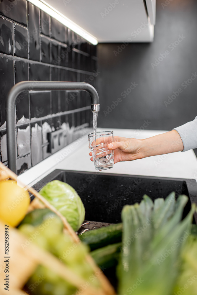 女人在厨房的饮水杯里装自来水。小时清洁饮用自来水的概念