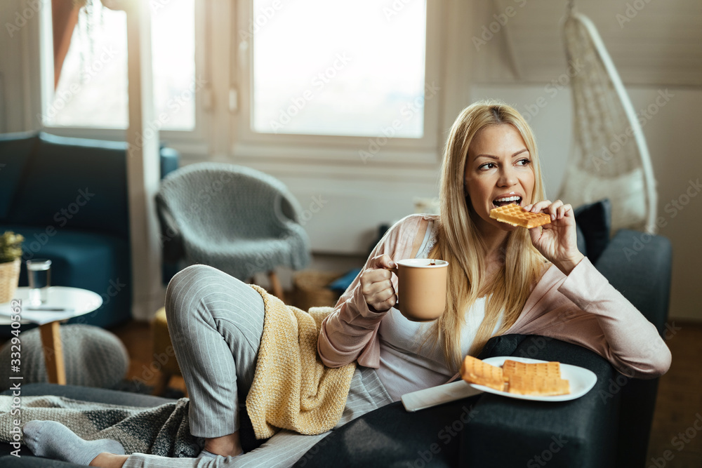 年轻女人在家放松时吃着华夫饼，喝着咖啡。