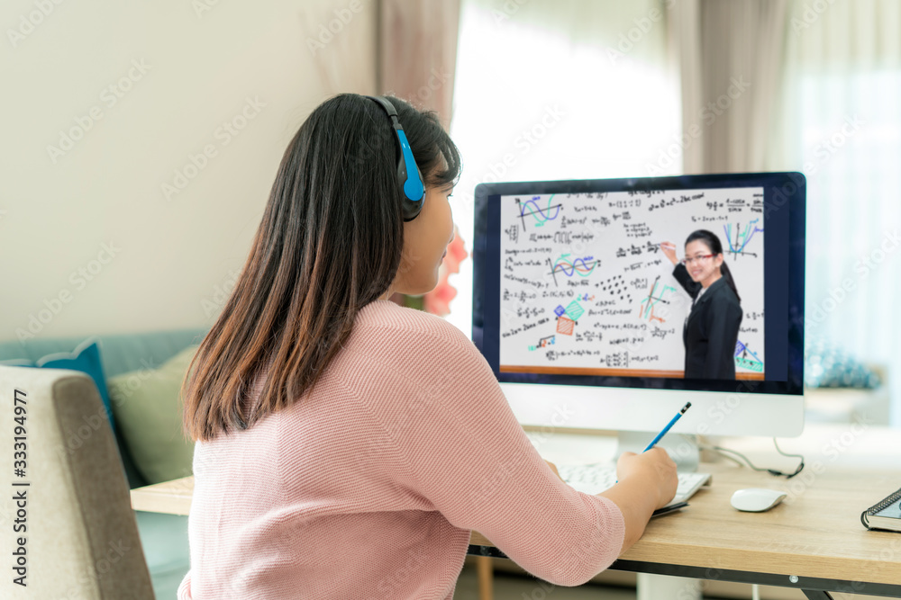 亚洲女学生与老师在家客厅的电脑上进行视频会议电子学习。e-l