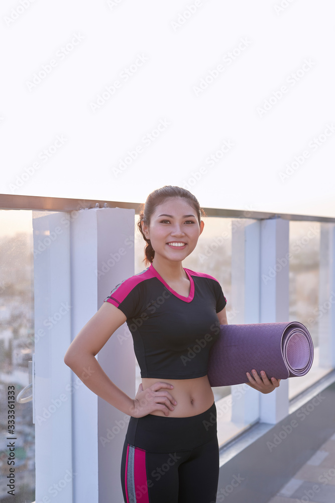穿着运动服的年轻美女拿着瑜伽垫