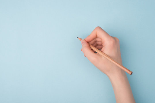 Top close up pov above overhead view photo of hand holding wooden pencil starting to draw a picture isolated over blue pastel color background