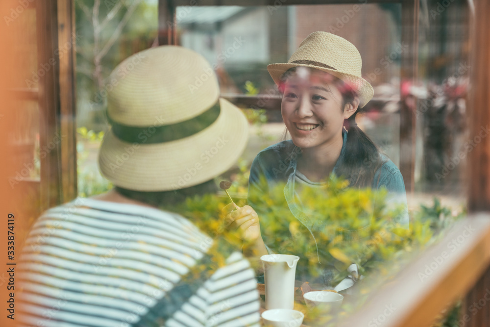 Group of asian female friends in straw hats sitting together at table by windows inside of japanese 