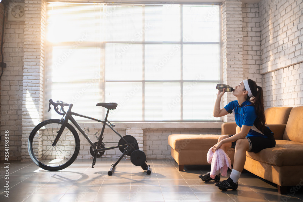 亚洲女自行车手。她在家里锻炼。在教练机上骑自行车，玩网上自行车