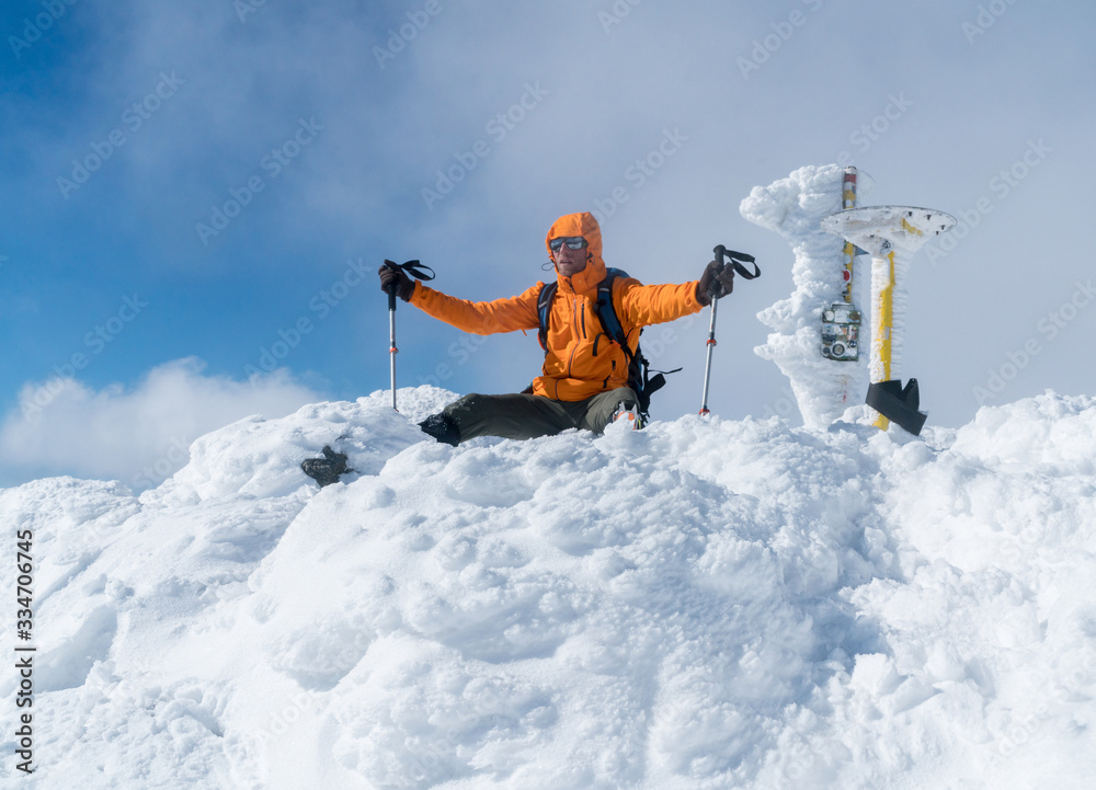 高山登山运动员在雪山顶峰穿着亮橙色软壳夹克。活跃的人们