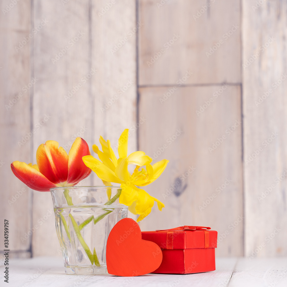 玻璃花瓶里的郁金香插花，带心形问候，木制桌子靠背上的喷壶装饰