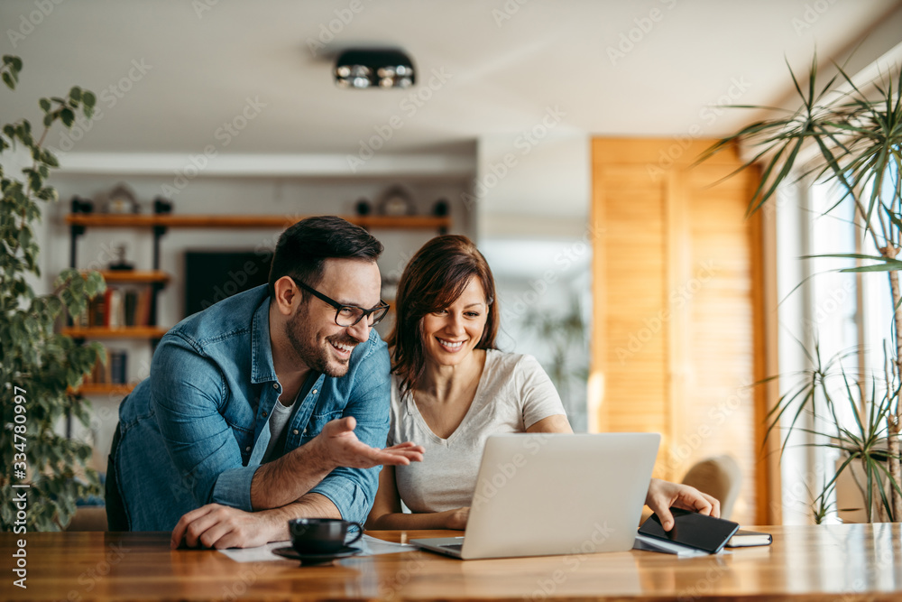 一对微笑的夫妇在舒适的家庭办公室里一起看着笔记本电脑的照片。