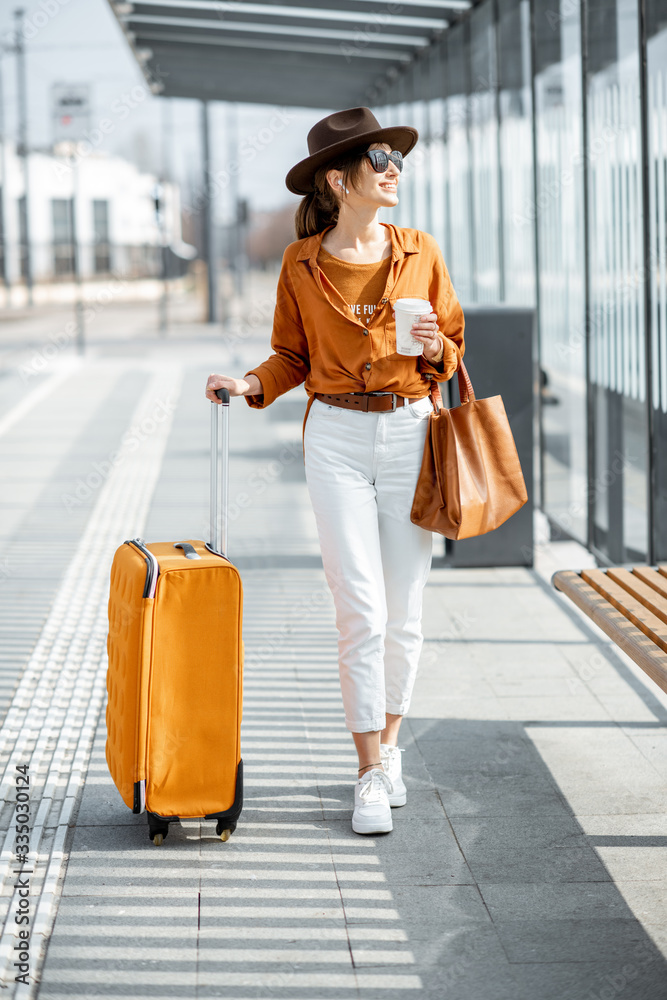 一位年轻的女性旅行者在公共交通站拿着行李和咖啡杯的随身行李