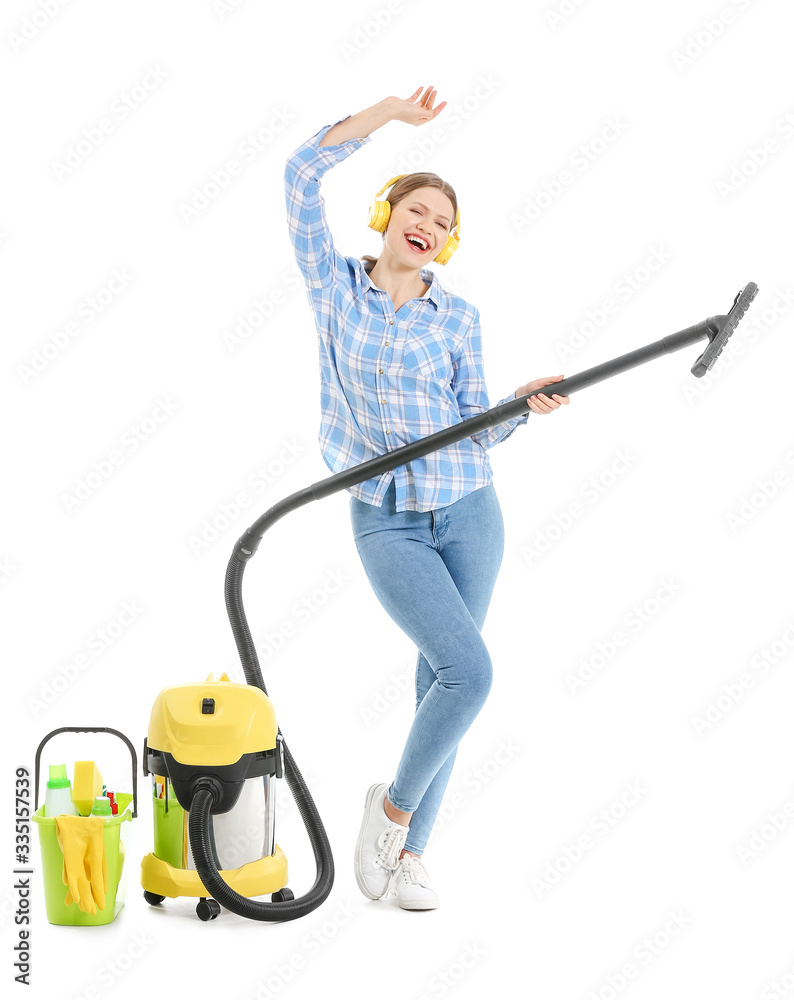 Young woman with vacuum cleaner listening to music on white background