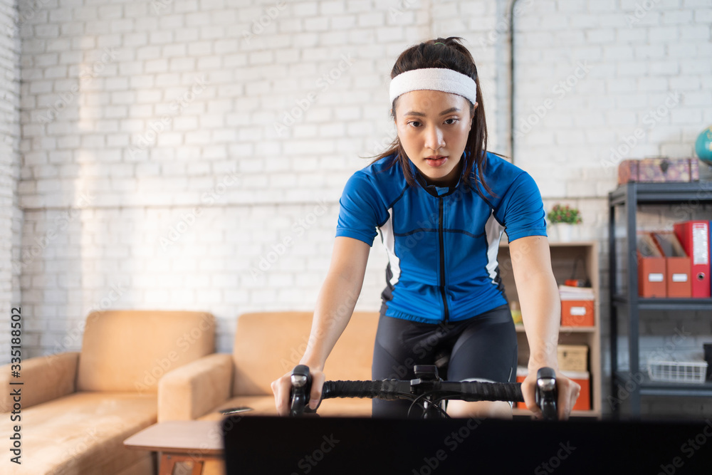 Asian woman cyclist. She is exercising in the house.By cycling on the trainer and play online bike g