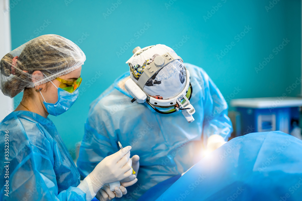 外科医生和他的助手在医院手术室做整形手术。外科医生戴着口罩
