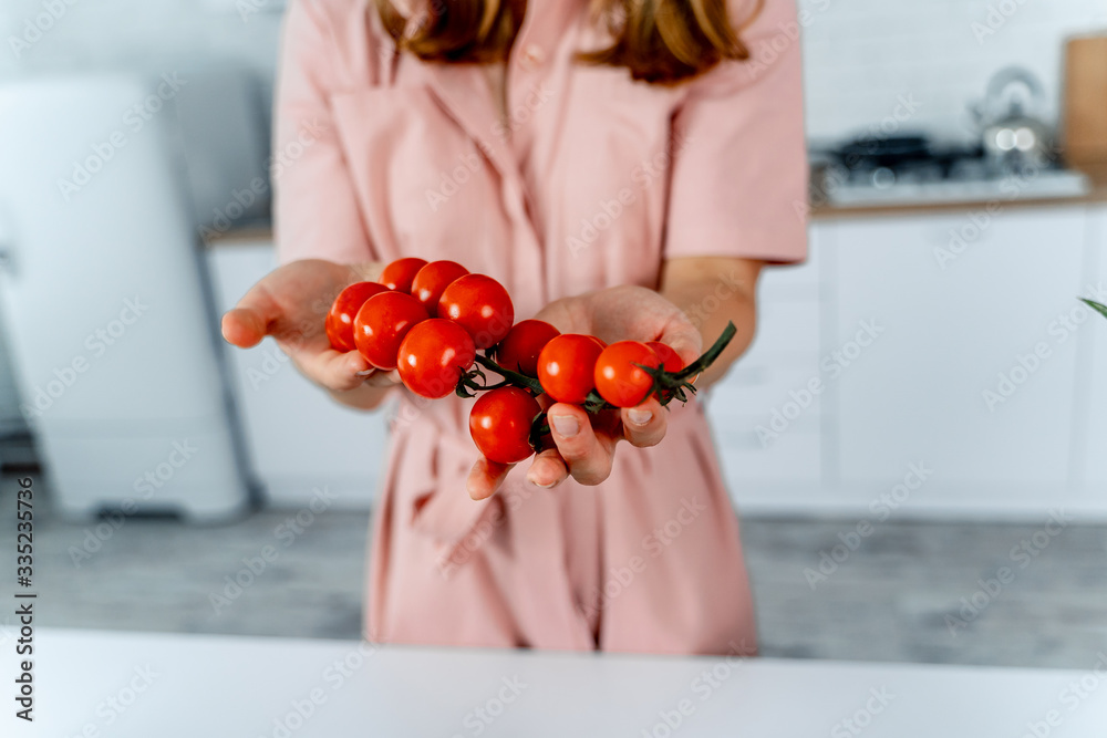 家庭主妇手里拿着成熟的樱桃番茄。厨房背景。女人穿的粉色连衣裙。家常菜c