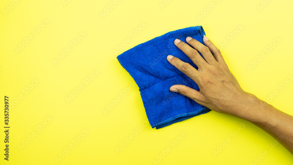 Man hand holding blue microfiber cleaning cloth isolated on yellow background.