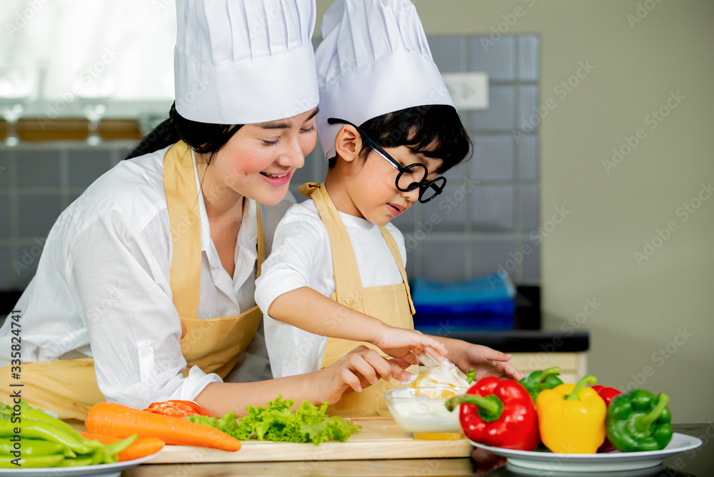 快乐可爱的亚洲小男孩，妈妈在家厨房准备烹饪新鲜沙拉