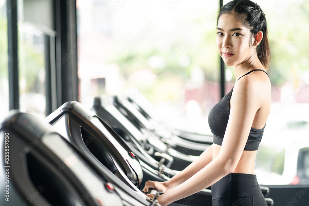 年轻健康的美丽亚洲女性在现代健身中在跑步机或跑步机设备上行走