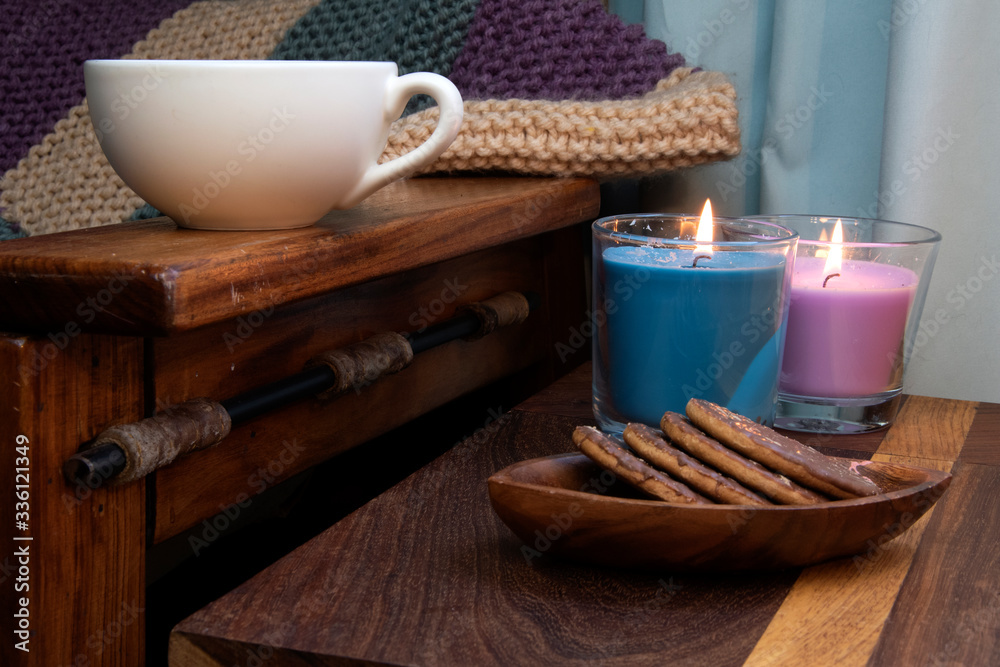 Cosy scene of chocolate biscuits, coffee, candles and wooden chair, rustic feeling