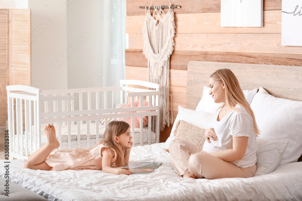 美丽的孕妇和她的小女儿在卧室看书