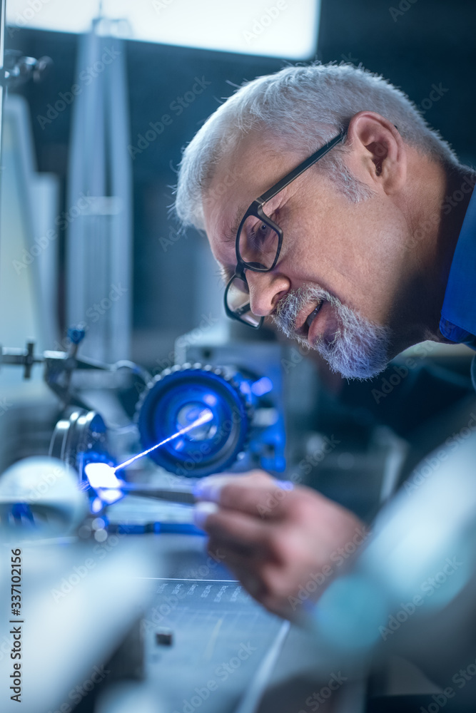 Close-up Portrait of Focused Middle Aged Engineer in Glasses Working with High Precision Laser Equip